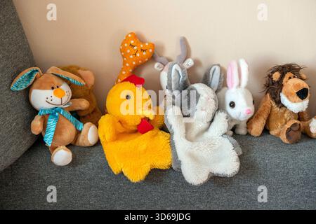 Una varietà di animali imbottiti colorati si siedono insieme su un divano grigio. La scena è luminosa e invitante, suggerendo un'atmosfera giocosa in un ambiente confortevole Foto Stock