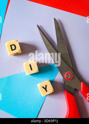 Disposizione verticale piatta di forbici e dadi con lettere che scrivono fai da te su carta colorata vivace Foto Stock