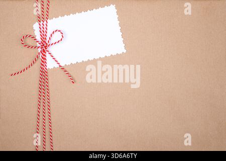 Corda di Natale rossa e bianca legata all'arco con etichetta bianca su sfondo Kraft Paper Foto Stock