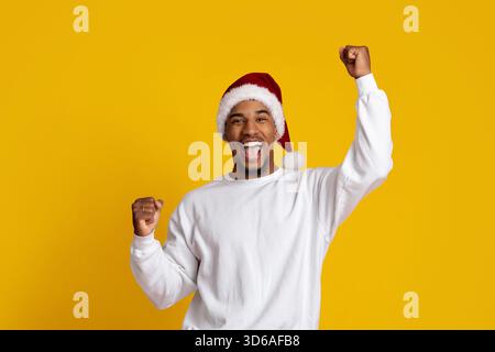 Joyful Man festeggia con Santa Hat su sfondo giallo brillante Foto Stock
