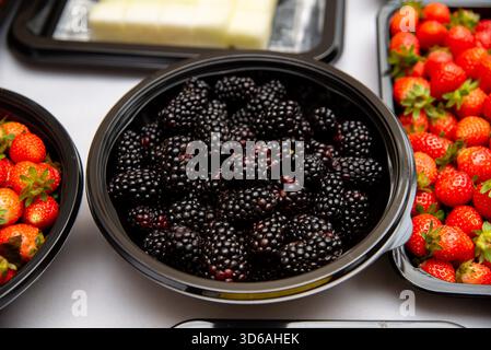 Una selezione di bacche fresche, tra cui more e fragole, visualizzate in una ciotola nera. ideale per temi alimentari e di stile di vita sano, con vi Foto Stock