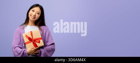 Una donna sorride mentre regge un regalo avvolto con un nastro rosso Foto Stock
