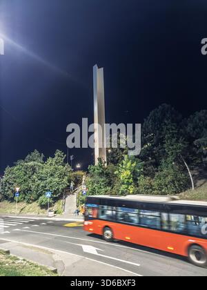 BELGRADO, SERBIA - 13 AGOSTO 2025: Un autobus urbano rosso passa accanto all'obelisco per i paesi non allineati di Belgrado, chiamato obelisco nesvrstanim zemljama Foto Stock