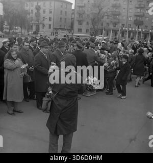 Slavyansk, Ucraina, URSS - 1970: Vivace scena d'archivio in Piazza della Rivoluzione d'ottobre durante la celebrazione del 7 novembre. I bambini delle scuole presentano fiori a funzionari e veterani, mentre un fotografo cattura il momento. I cittadini sono vestiti con cappotti caldi e cappelli per il freddo autunno. Edifici residenziali sovietici sono sullo sfondo. Questa immagine in bianco e nero riflette l'atmosfera festosa, lo spirito della comunità e le tradizioni della regione di Donetsk durante la pacifica era sovietica. Foto Stock