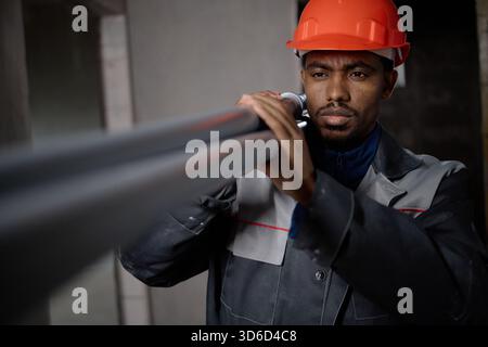 Giovane uomo nero adulto che installa tubi indossando un elmetto protettivo Foto Stock