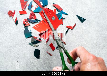 una mano con le forbici che tagliano le carte di plastica in piccoli pezzi Foto Stock