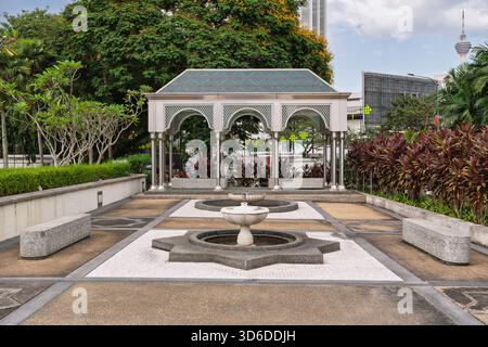 Moderno padiglione islamico e fontana presso la Moschea Nazionale di Kuala Lumpur, Malesia. KL Tower sullo sfondo, circondato da lussureggianti giardini tropicali sotto un cielo nuvoloso Foto Stock
