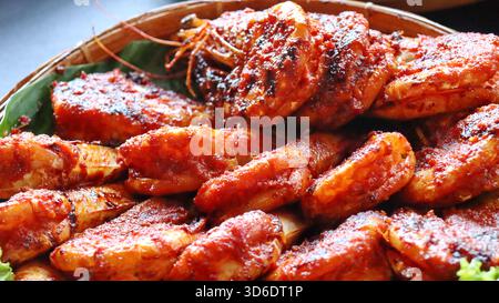 Gamberi grigliati speziati indonesiani ricoperti di salsa al peperoncino rosso, serviti su foglie di banana nel cestino di bambù. Autentica cucina asiatica a base di pesce, tradizionale Foto Stock