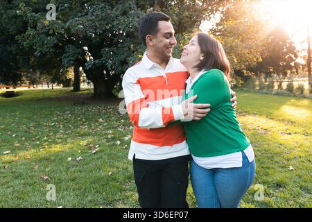 Giovane coppia latina che abbraccia e sorride in un parco durante il tramonto Foto Stock