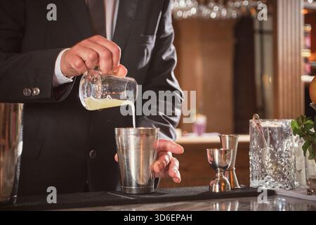 Coltivare un barman anonimo che versa un cocktail fresco dal matraccio nello shaker al bancone del bar Foto Stock