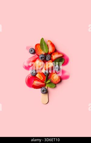 Un'immagine vivace che mostra un papavero di frutta a metà fusione con fragole e mirtilli su un morbido sfondo rosa. Foto Stock