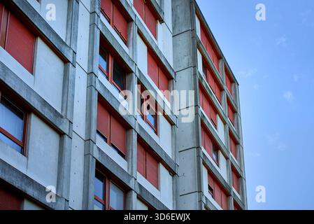 Edificio brutalista in cemento a Kaiseraugst, Svizzera, caratterizzato da linee geometriche e persiane rosse per finestre, che mostrano simmetria urbana e design funzionale Foto Stock