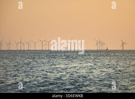 Le turbine eoliche offshore, i parchi eolici si trovano in mare al tramonto, simboleggiando l'energia pulita, la sostenibilità e le risorse rinnovabili con un oceano tranquillo Foto Stock