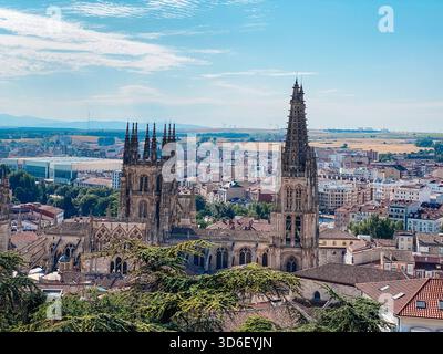 Le torri gotiche della Cattedrale di Burgos, in Spagna, si innalzano in alto sul centro storico, circondate dai tetti della città, da colline lontane e da un'estate luminosa Foto Stock
