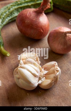 bulbo d'aglio rotto con cipolle rosse su tavola di legno, verdure verdi sullo sfondo, messa a fuoco morbida, ingredienti di cottura sani e concetto culinario Foto Stock