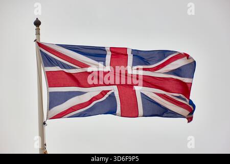 Bandiera Union Jack in volo sul palo contro Bright Sky, simbolo della Gran Bretagna e orgoglio Foto Stock