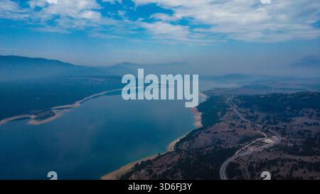 Ampia ripresa di un grande lago artificiale e di colline aride e ondulate che creano una prospettiva spettacolare che sfuma nell'orizzonte nebbioso ad alta quota Foto Stock