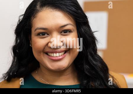 Donna d'affari che indossa un blazer marrone sorridente mentre si trova in ufficio con un cordoncino e una collana Foto Stock