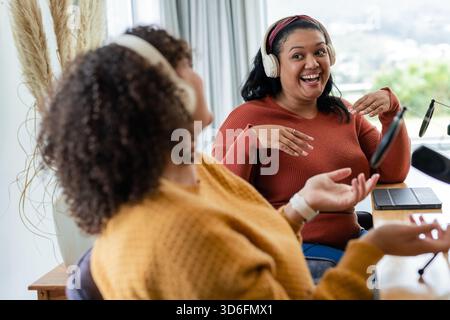 Diverse amiche che registrano podcast in studio domestico con microfoni, cuffie, tablet, notebook Foto Stock