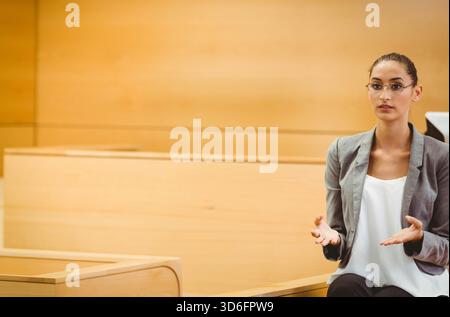 Donna seduta sulla panchina uditiva, gestante, che parla al leggio con occhiali blazer grigi, spazio fotocopie. Tribunale, podio, presentazione, legno, interni, Foto Stock