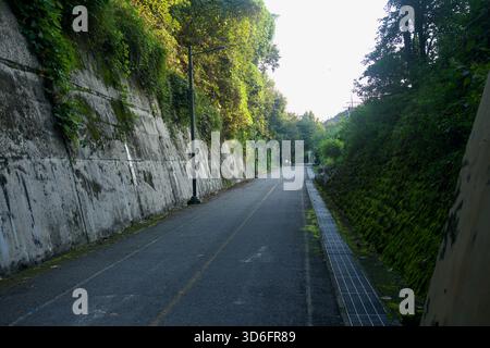 Un tratto rettilineo del percorso ciclabile di Bukhangang corre tra le pareti di contenimento in cemento a Namyangju, con muschio e griglie di drenaggio che rivestono l'ombreggiato Foto Stock