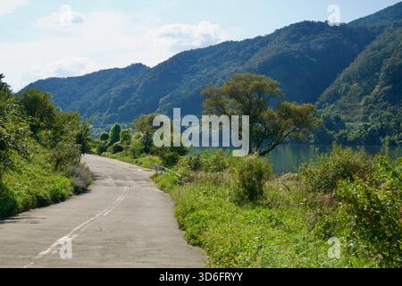 Un albero solitario si erge accanto ad un'ampia curva del fiume dove il Bukhangang incontra pendii boscosi, con una leggera retroilluminazione sull'acqua e una curva di corsia ruvida Foto Stock