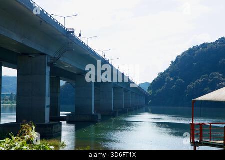 Moli di cemento e scale di manutenzione del Ponte di Kyunggang si innalzano sulla calma Bukhangang, con colline boscose che si innalzano sul lato Chuncheon del fiume. Foto Stock