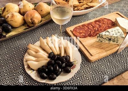 Formaggi assortiti, frutta, salumi, patatine e vino bianco disposti su un tavolo, perfetti per il cibo e lo stile di vita Foto Stock