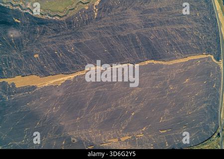 Foto aerea dall'alto verso il basso di una vasta terra scura, probabilmente bruciata o danneggiata, con una linea orizzontale di barba corta dorata. Immagine concettuale dell'impatto della zona di guerra e del degrado ambientale. Foto Stock