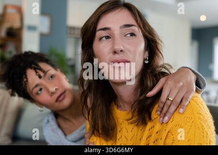 Diverse amiche si siedono sul divano nel soggiorno e indossano un maglione in maglia gialla con cuscini Foto Stock