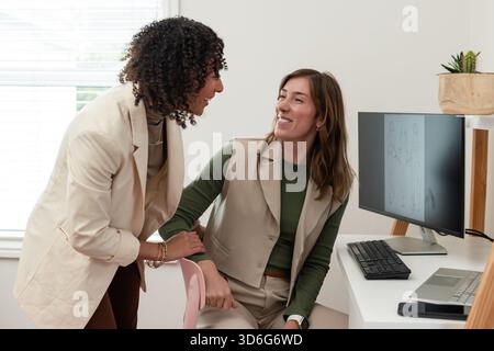 Diverse collaboratrici che si appoggiano alla scrivania bianca in ufficio per rivedere gli schizzi sulle apparecchiature informatiche Foto Stock