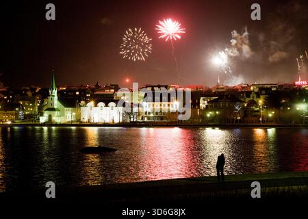 Fuochi d'artificio la vigilia di Capodanno a mezzanotte. Lago Tjornin, centro di Reykjavik, Islanda. Foto Stock