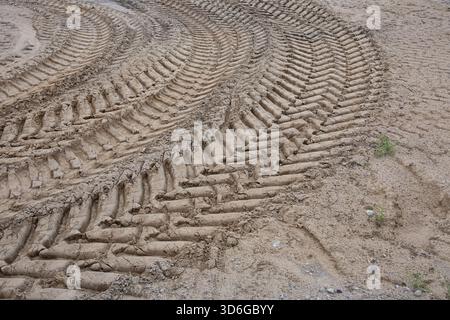 Cingoli di pneumatici freschi provenienti da macchinari per l'edilizia pesanti impressi su terreno asciutto, che formano schemi curvi in un cantiere edile Foto Stock