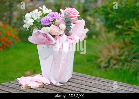 Un bouquet di fiori diversi con una barretta di cioccolato su un tavolo di legno di fronte al prato verde nel giardino Foto Stock