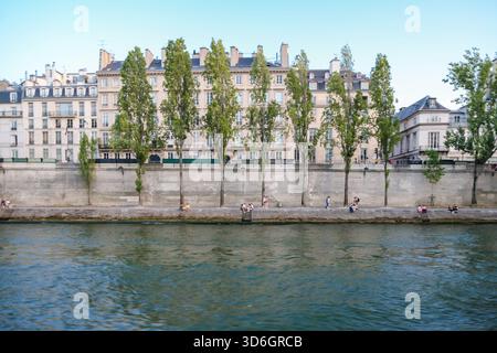 Scena sul lungofiume lungo la Senna a Parigi, con le classiche facciate degli appartamenti e i pedoni che camminano lungo l'argine. Foto Stock