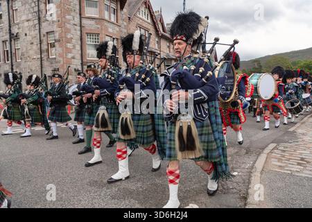 I Pipers suonano con la Massed Pipe Band mentre marciano attraverso il villaggio di Braemar durante il Braemar Gathering su Royal Deeside Foto Stock