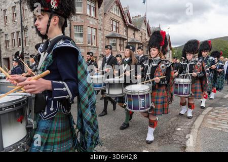 I ruspi marciano attraverso il villaggio di Braemar con le bande di tubo massaggiato mentre si dirigono verso il raduno di Braemar Foto Stock