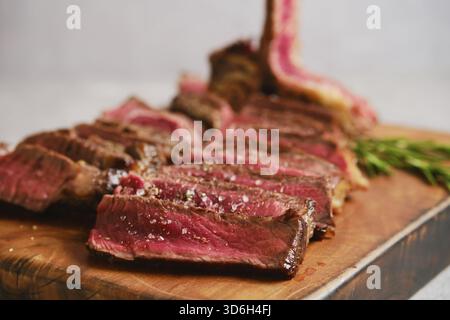 Vista ravvicinata della bistecca grigliata a fette media rara su un tagliere di legno. La carne è perfettamente cotta con un succoso centro rosa. Erbe fresche Foto Stock