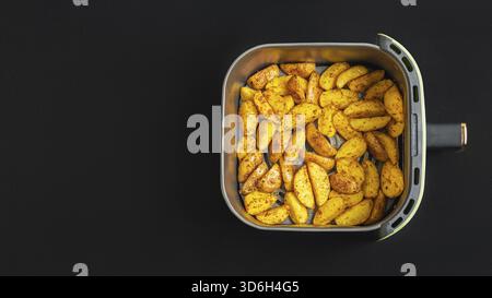 Vista dall'alto delle patate dorate in un cestello della friggitrice ad aria su uno sfondo scuro. Questi spicchi sapientemente stagionati sono perfetti per spuntini o. Foto Stock