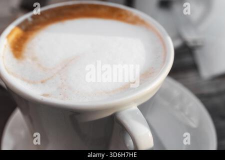 Primo piano del cappuccino appena preparato con latte schiumoso servito in una tazza di ceramica bianca, che mostra un leggero vortice di caffè lungo il bordo Foto Stock
