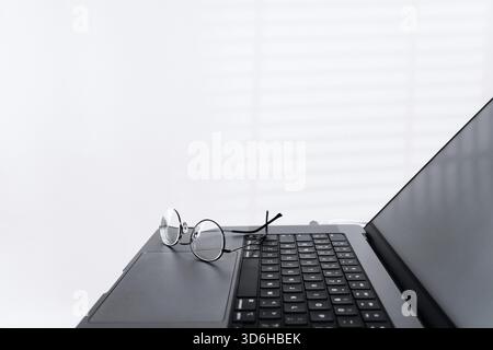 Vista laterale ritagliata del computer portatile con occhiali in un ufficio leggero. Moderno spazio di lavoro per programmatori, designer o freelance. Lavoro remoto online, dist Foto Stock