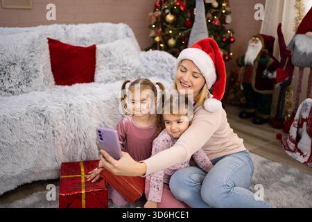 Madre e figlie si fanno selfie vicino all'albero di Natale Foto Stock