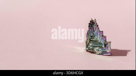 BismuthumCrystal sintetico in bismuto con pellicola di ossido di iridescenza su sfondo rosa primo piano isolato. Incredibile colorata scintillante arcobaleno Bismuth Gemstone mi Foto Stock