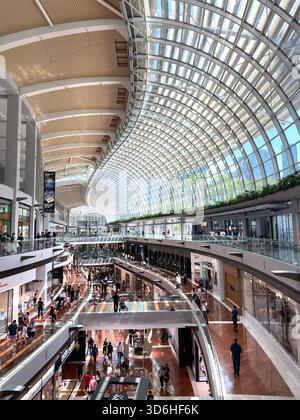 Vista interna di un moderno centro commerciale a più piani con tetto ad arco in vetro, negozi di lusso e persone che camminano lungo i corridoi Foto Stock