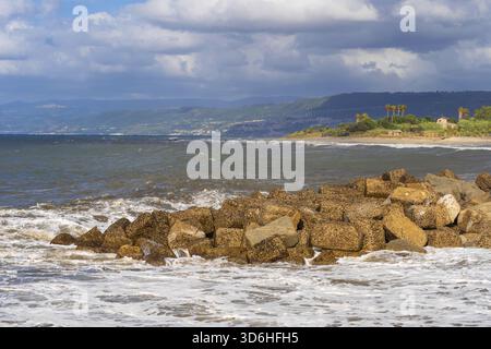 Un'onda potente si schianta sulla costa rocciosa con acqua bianca schiumosa che schizza contro le rocce. La scena dinamica cattura l'energia e il movimento di Ocean ag Foto Stock