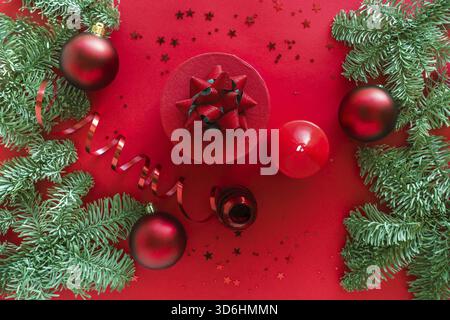 Composizione natalizia composta da regalo natalizio, candela, rami di pino, baule su superficie rossa. buon natale e felice anno nuovo. Piatto, superiore Foto Stock