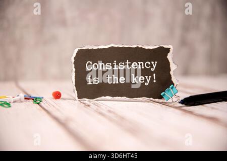 Un pezzo di carta rivestita con la consistenza scritta a mano è la chiave fissata con nastro su una superficie a grana di legno. La carta ha un bordo strappato e una fila di "ho" Foto Stock