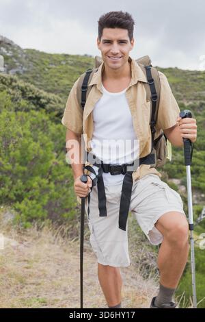 Adulto maschio escursionista in piedi su un sentiero roccioso, con pali da trekking, camicia beige e zaino. All'aperto, natura, robusto, cresta, sentiero, coperto, a Foto Stock