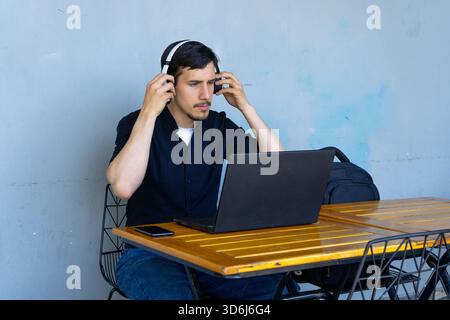 Uomo che trova concentrazione e produttività indossando le cuffie mentre lavora su un notebook in un bar o in un'area di lavoro all'aperto Foto Stock