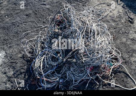 Un grande e aggrovigliato mucchio di cavi e fili elettrici isolati raccolti separatamente su terreno scuro, pronti per essere trattati per il riciclaggio dei metalli. Foto Stock